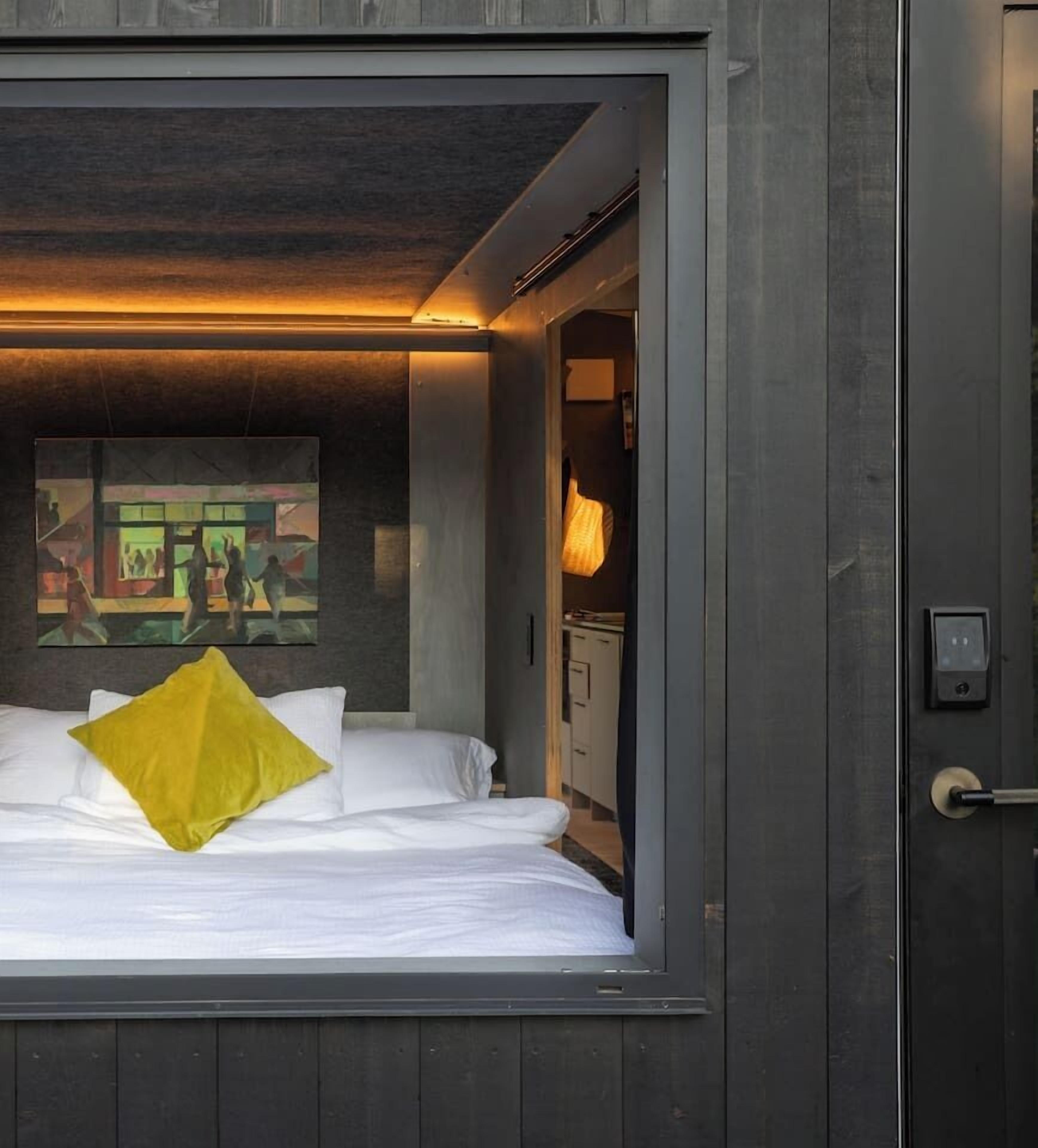 Une chambre d’hôtel moderne, avec un lit, un tableau au mur et une porte dotée d’une poignée.
