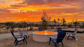 A circular fire pit surrounded by chairs, set against a sunset with mountains in the background. - Baja Toscana Rancho Olivares (Valle de Guadalupe)