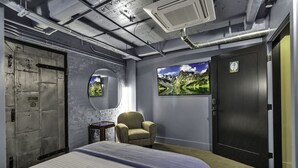 Una habitación de hotel con una cama, una silla, un espejo redondo y dos cuadros en la pared.