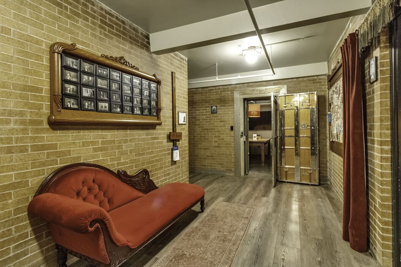 A room with a brick wall, a red sofa, a framed photo display, and a door leading to another room.