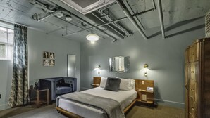 A hotel room with a bed, bedside tables, a desk, and a wardrobe. - The Dillinger Room @ The Bank (East Aurora)