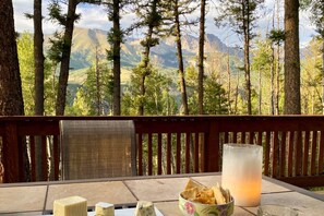 Una mesa con una vela, un recipiente con aperitivos y un vaso de agua, con un bosque y montañas de fondo.