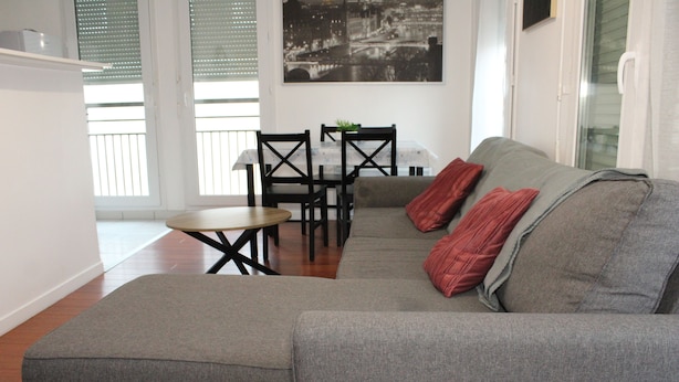 A living room with a grey sofa, two red pillows, a small wooden table, and black chairs. - Beautiful apartment in Meaux, 15 minutes from Disneyland (Meaux)