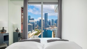 A hotel room with a bed, pillows, a lamp, and a view of a cityscape and marina. - LUX 52 42 Deluxe Marina View Suite 3 (Dubai)