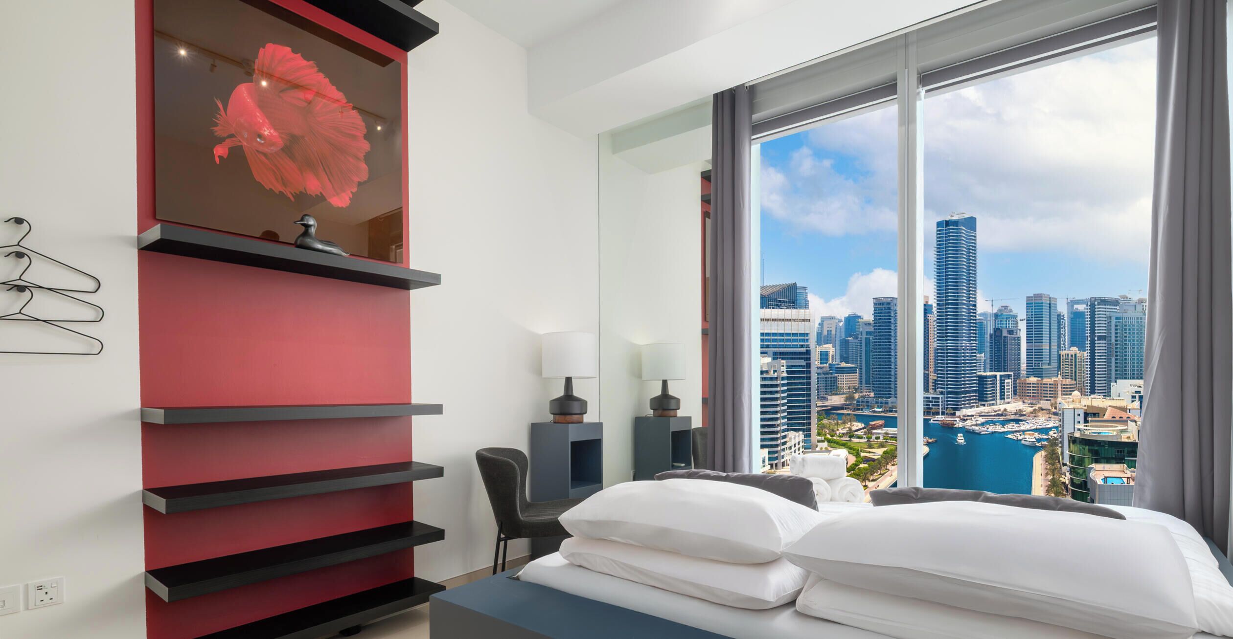 Ein modernes Hotelzimmer mit einem großen Bett, einer roten und schwarzen Regaleinheit und Blick auf die Stadt.