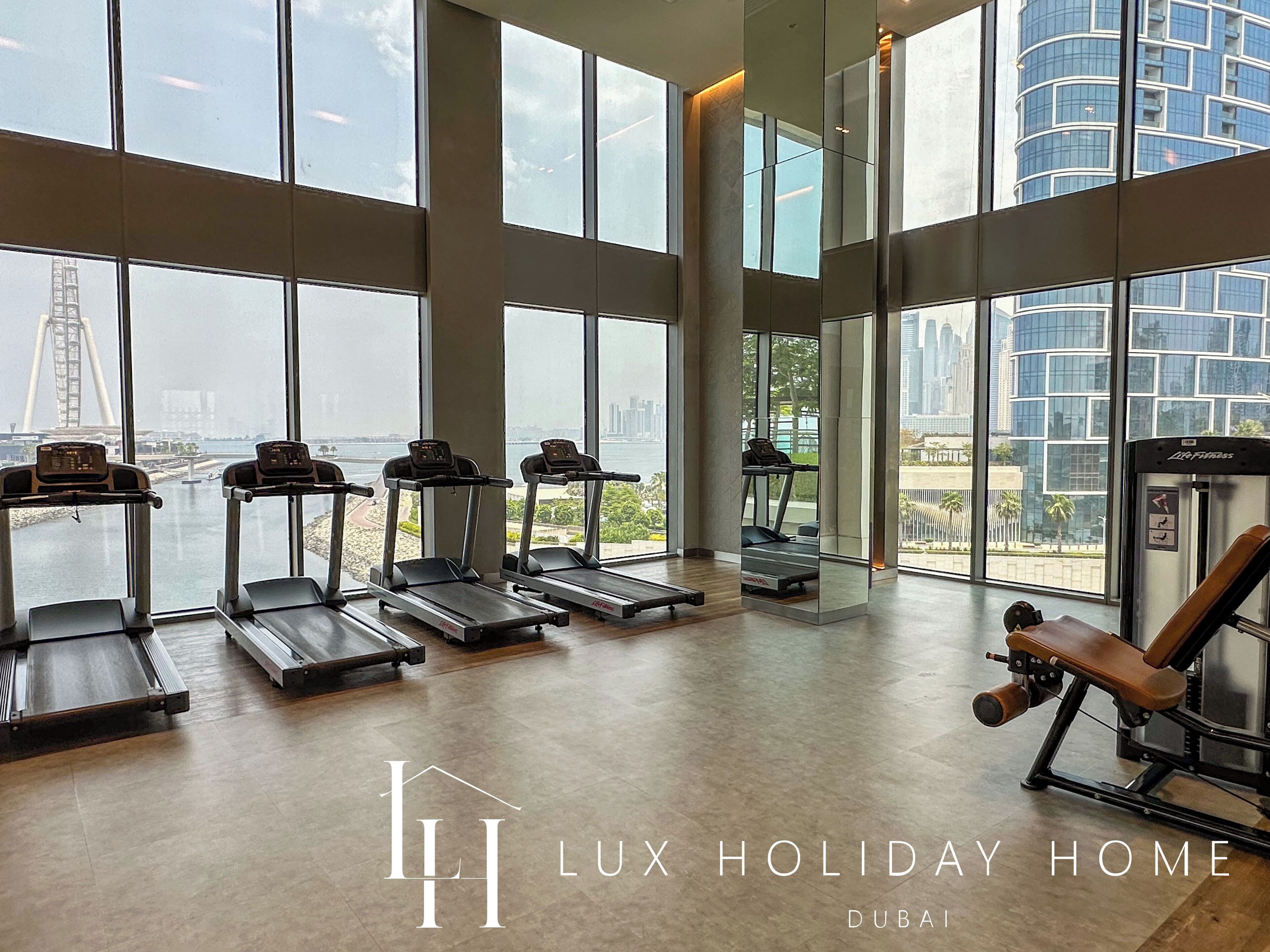 A spacious gym with treadmills, a bench press, and large windows offering views of a cityscape and a bridge.
