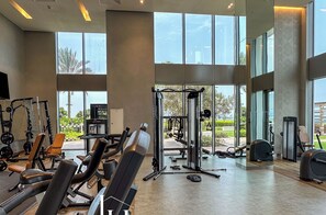 Ein geräumiges Fitnessstudio mit verschiedenen Trainingsgeräten, großen Fenstern und Blick ins Freie.