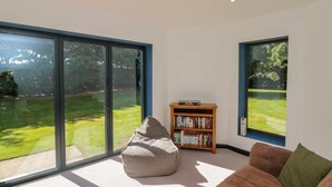 Un salon moderne avec de grandes fenêtres, un fauteuil poire, une bibliothèque et un canapé marron.