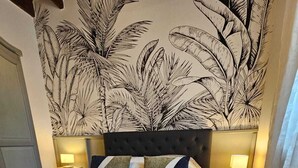 A hotel room with a large bed, a headboard with a leaf pattern, two bedside tables with lamps, and a curtain on the window.