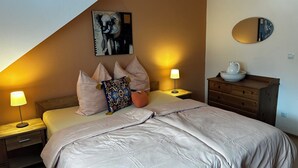 A bedroom with a bed, two bedside lamps, a nightstand, a dresser, a mirror, and a painting on the wall. - Olivia Vacation Rental in Hönow (Hoppegarten)