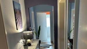A hallway with a wooden floor, a white dresser, a lamp, and a door leading to another room. - Olivia Vacation Rental in Hönow (Hoppegarten)