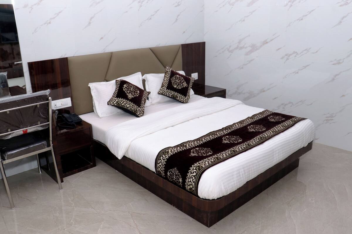 Una cama bien hecha con cabecera, dos almohadas, una mesita de noche con teléfono y un televisor fijado a la pared.