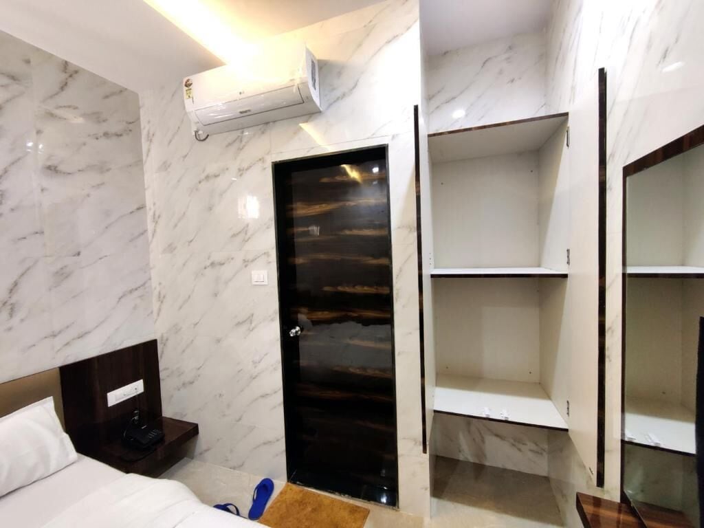 Habitación de hotel con pared de mármol, cama, armario y puerta con detalles en madera oscura.