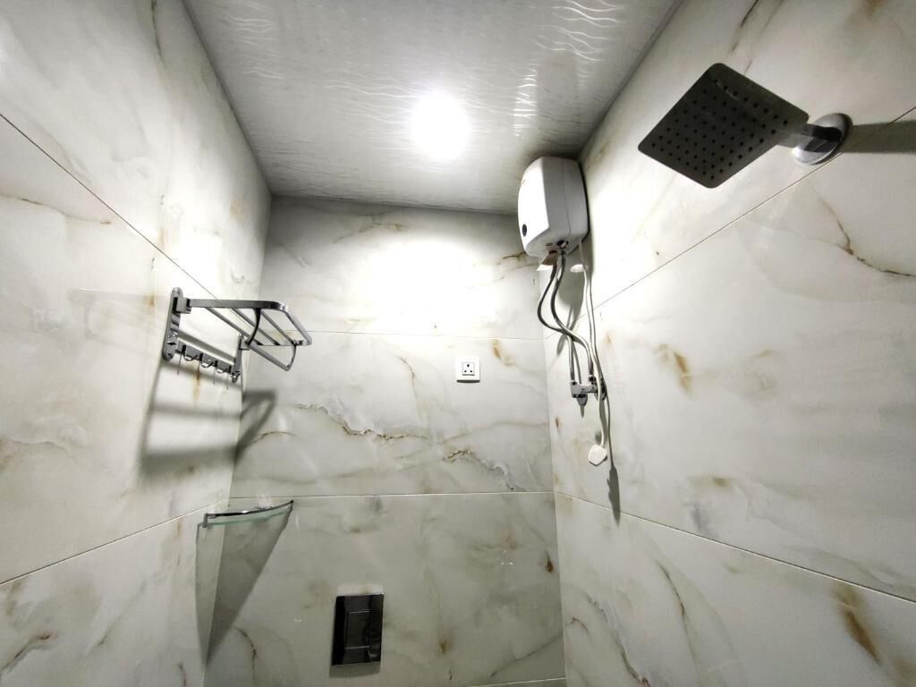 A bathroom with marble walls, a showerhead, a glass shower enclosure, and a towel rack.