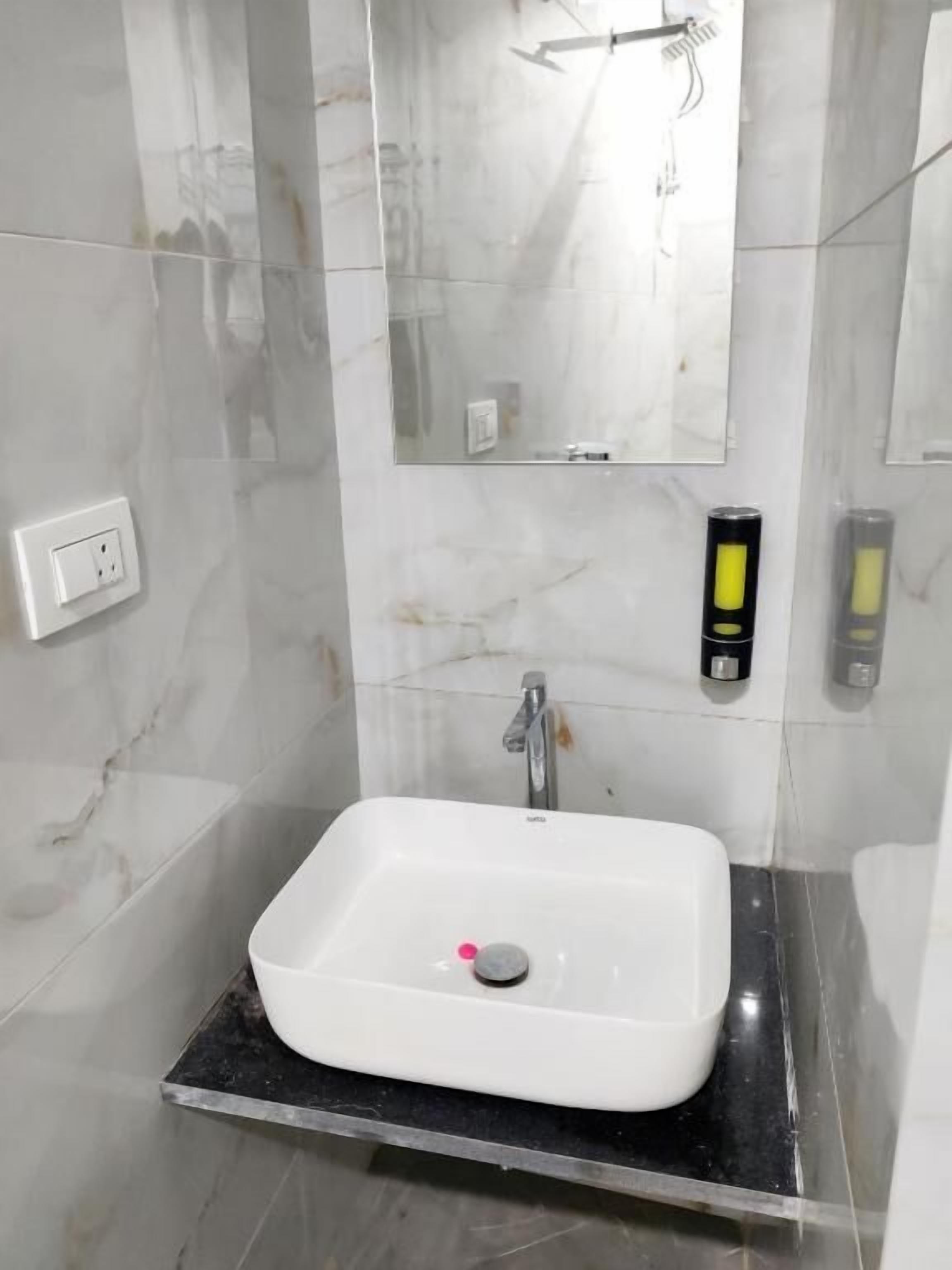 A bathroom with a white sink, a mirror, a faucet, and a soap dispenser.