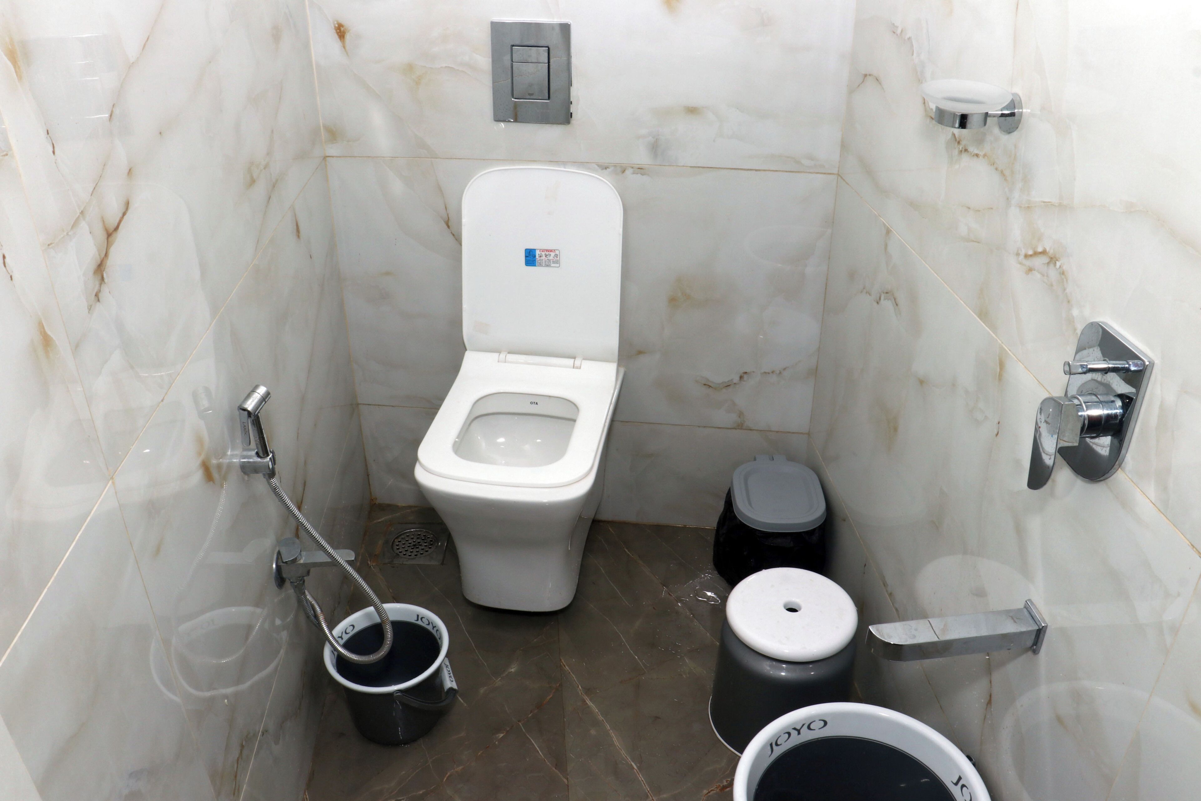 A small, compact bathroom with a toilet, bidet, and two trash bins.