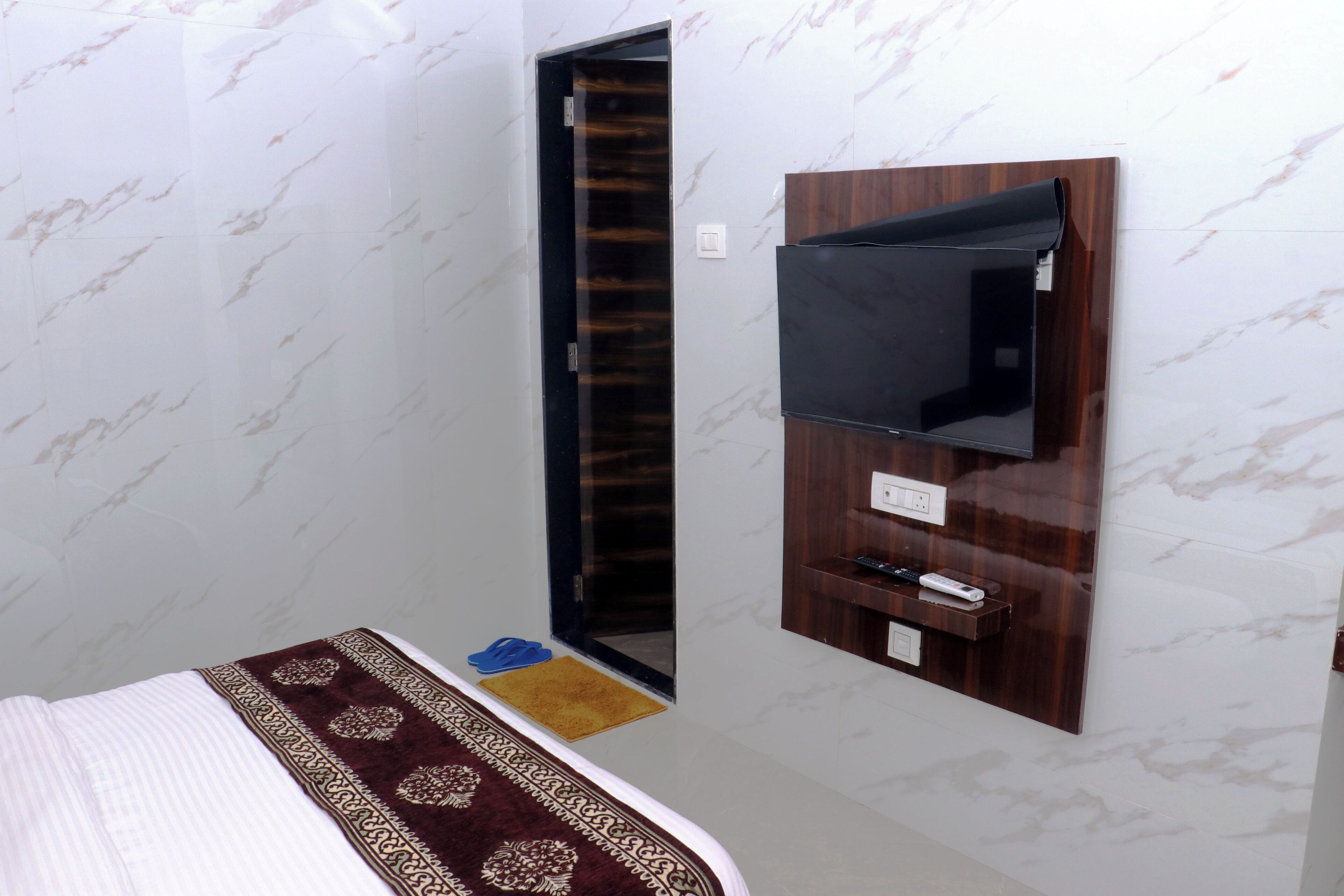 A hotel room with a bed, a TV mounted on the wall, a door, and a small rug.