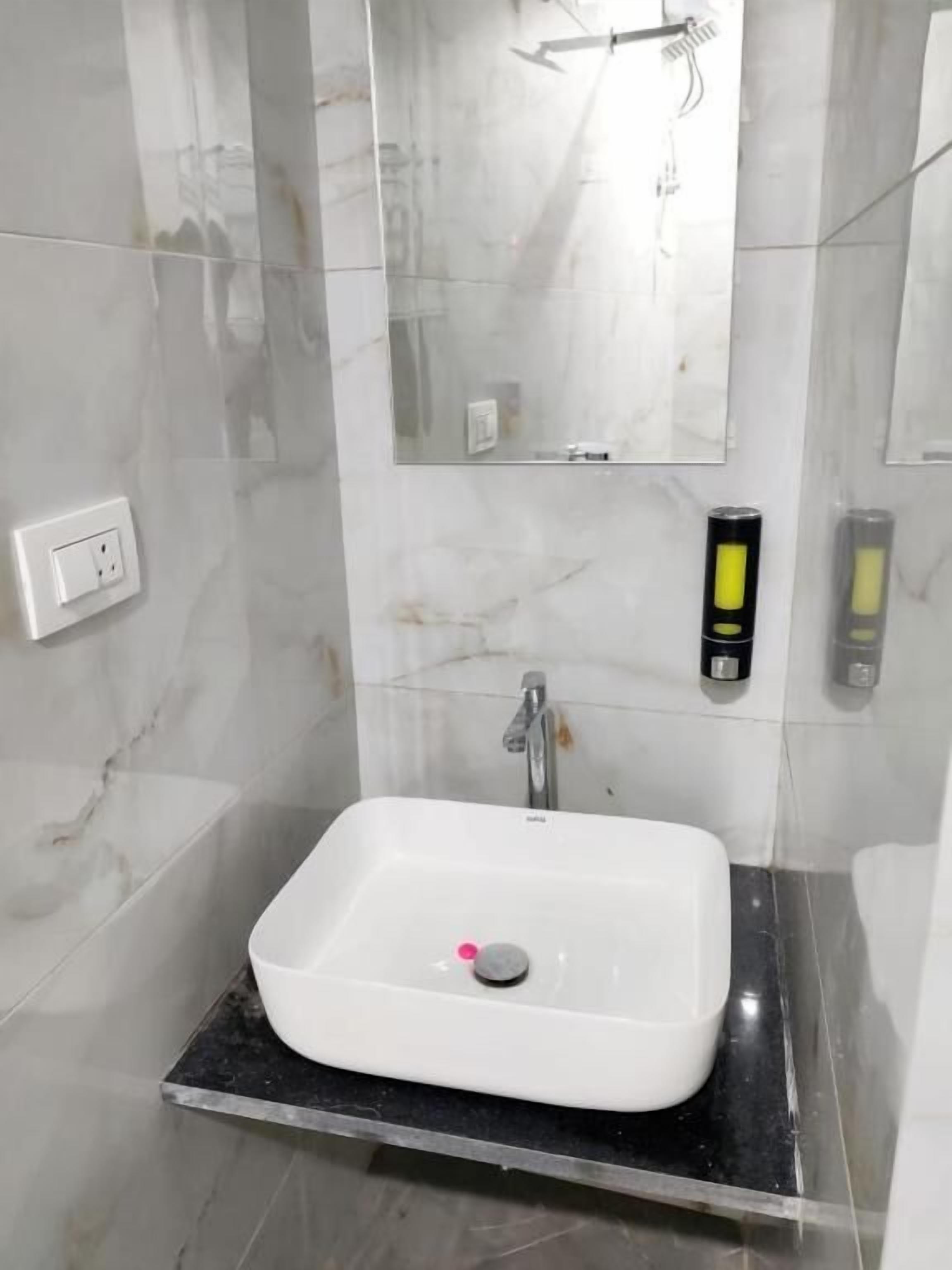 A bathroom with a white sink, a mirror, a faucet, and a soap dispenser.