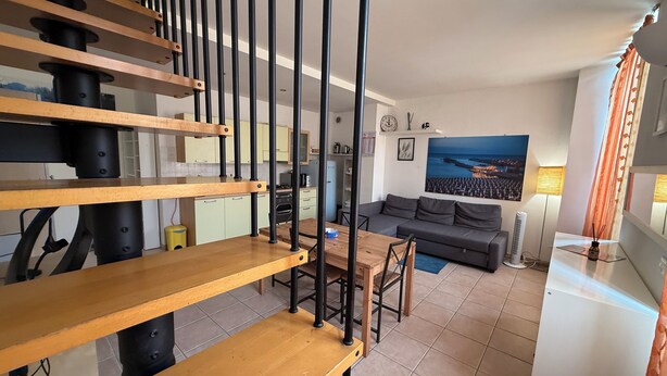 A modern interior with a staircase, a dining area, a sofa, and a kitchen.