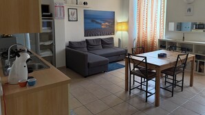 A compact living space with a kitchenette, a sofa, a dining table with chairs, and a large window with curtains.
