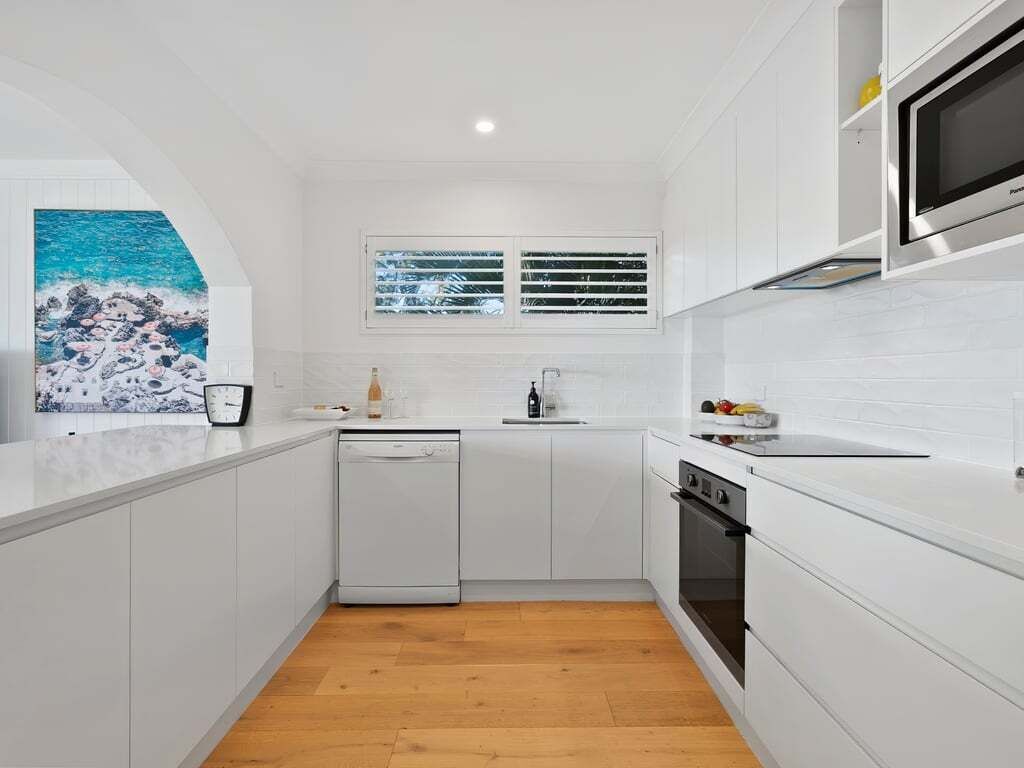 Una cocina moderna con armarios blancos, lavavajillas, horno y una ventana con persianas.