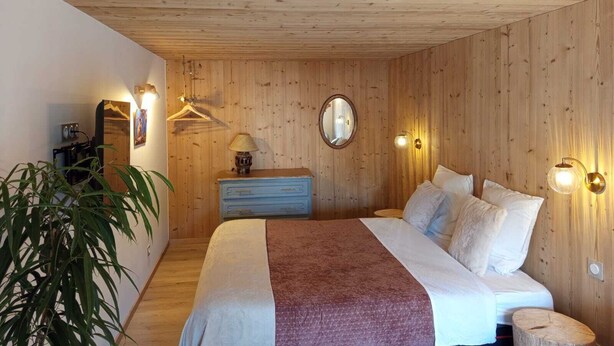 A wooden-paneled bedroom with a bed, bedside lamps, a dresser, a mirror, and a hanging light. - Au Mont Chablis (Champagnole)