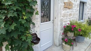 A stone building with a white door, a metal gate, and potted plants with pink flowers. - Au Mont Chablis (Champagnole)