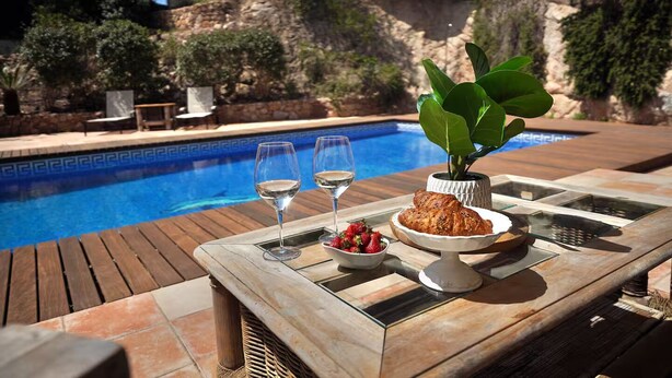 A poolside table with two wine glasses, a bowl of strawberries, a croissant, and a potted plant. - Spacious 4BR Villa w/ AC, Private Pool, BBQ & Sea Views – Costa Brava (Sant Feliu de Guíxols)