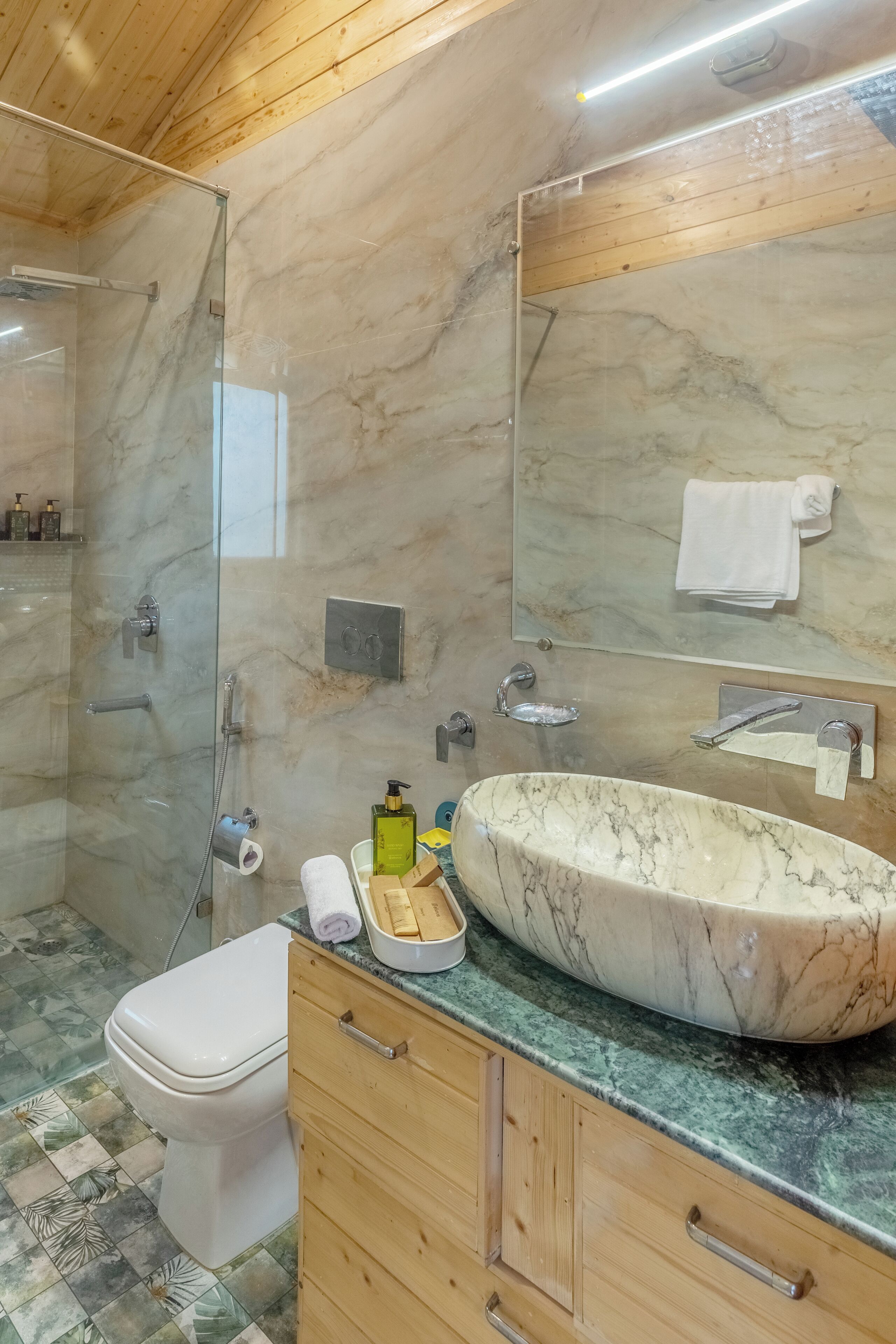 A bathroom with a glass-enclosed shower, a white toilet, a marble sink, and wooden cabinets.