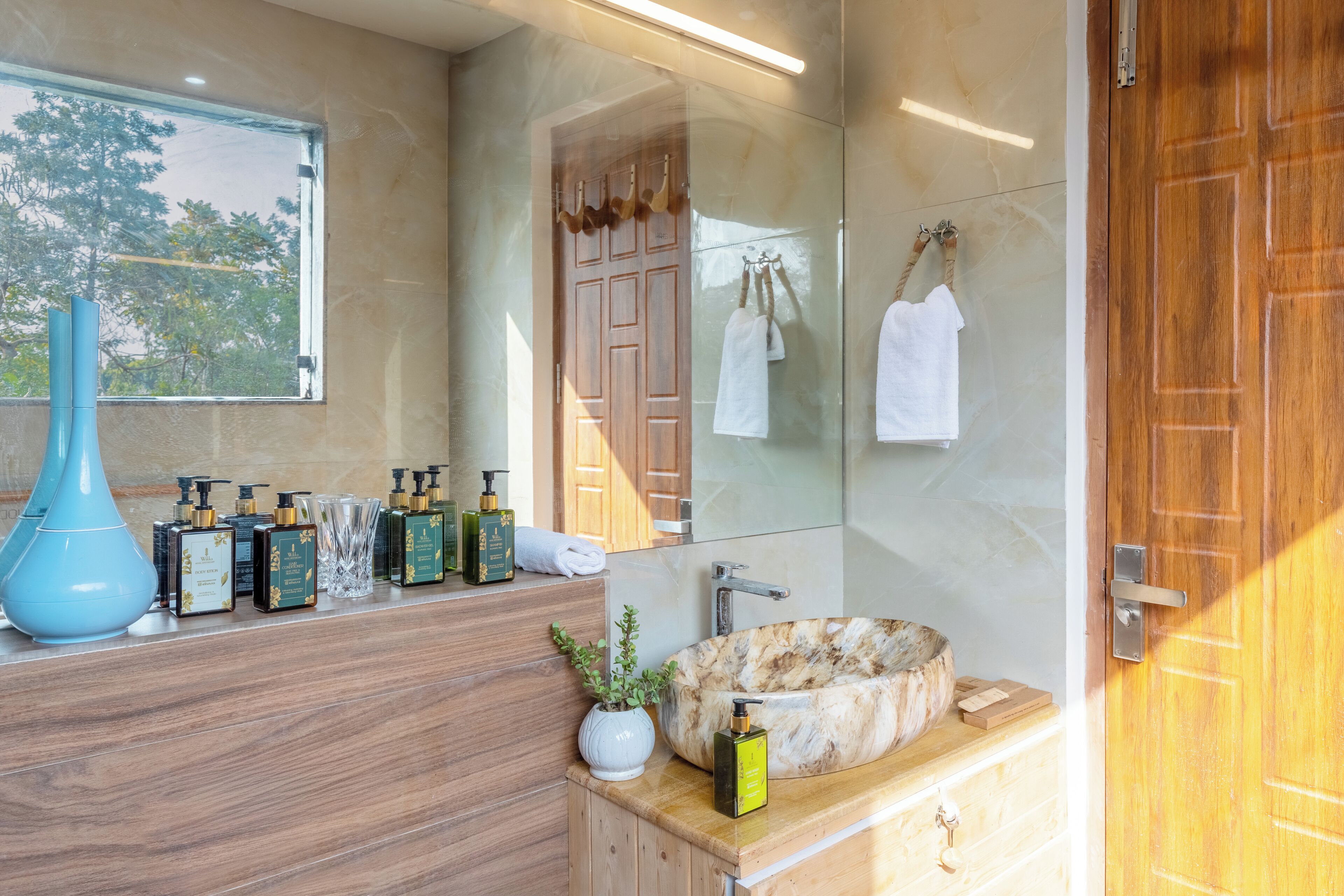 Un baño con tocador de madera, un espejo grande, lavamanos de mármol y varios artículos de aseo.