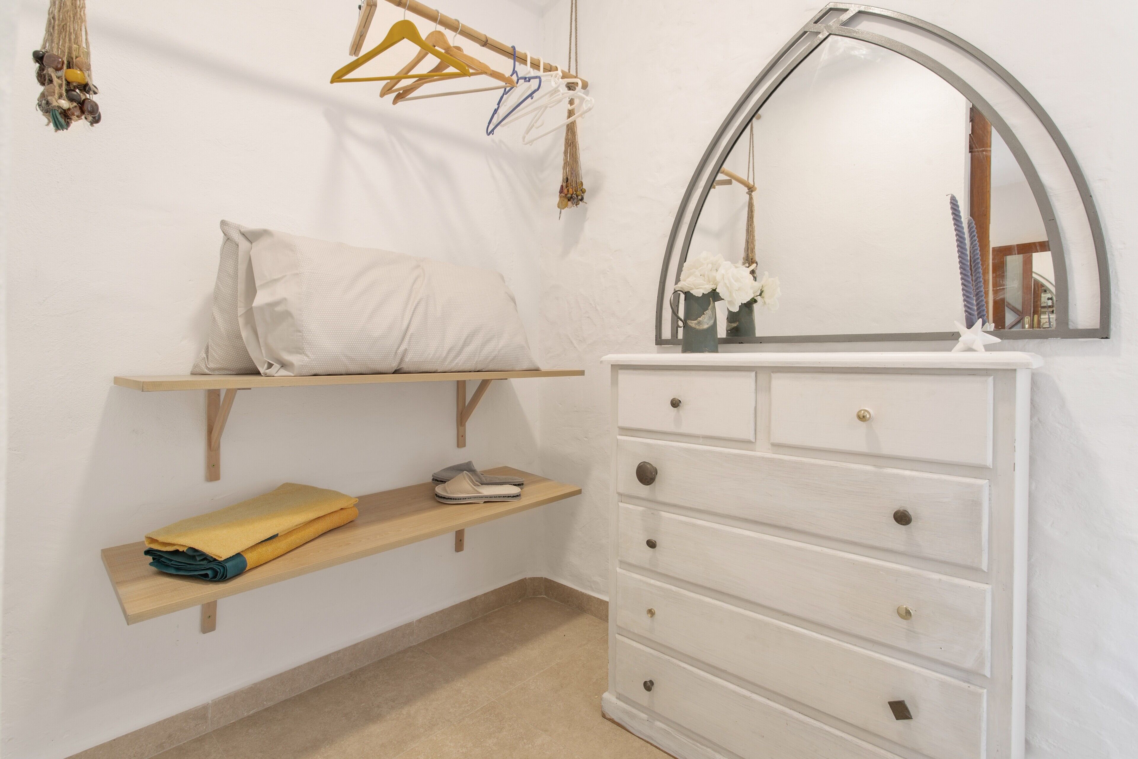 Un dormitorio con cama, cómoda, espejo y estante con ropa doblada y un zapato.