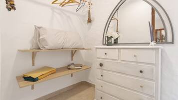 Un dormitorio con cama, cómoda, espejo y estante con ropa doblada y un zapato.