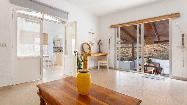 A spacious room with a wooden table, a yellow vase, and a view of a desert landscape through large sliding glass doors. - Holiday Home 'Casa Azul' with Sea View, Private Terrace & Wi-Fi (Las Palmas)