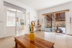 Et rummeligt værelse med et træbord, en gul vase og udsigt over et ørkenlandskab gennem store skydedøre.