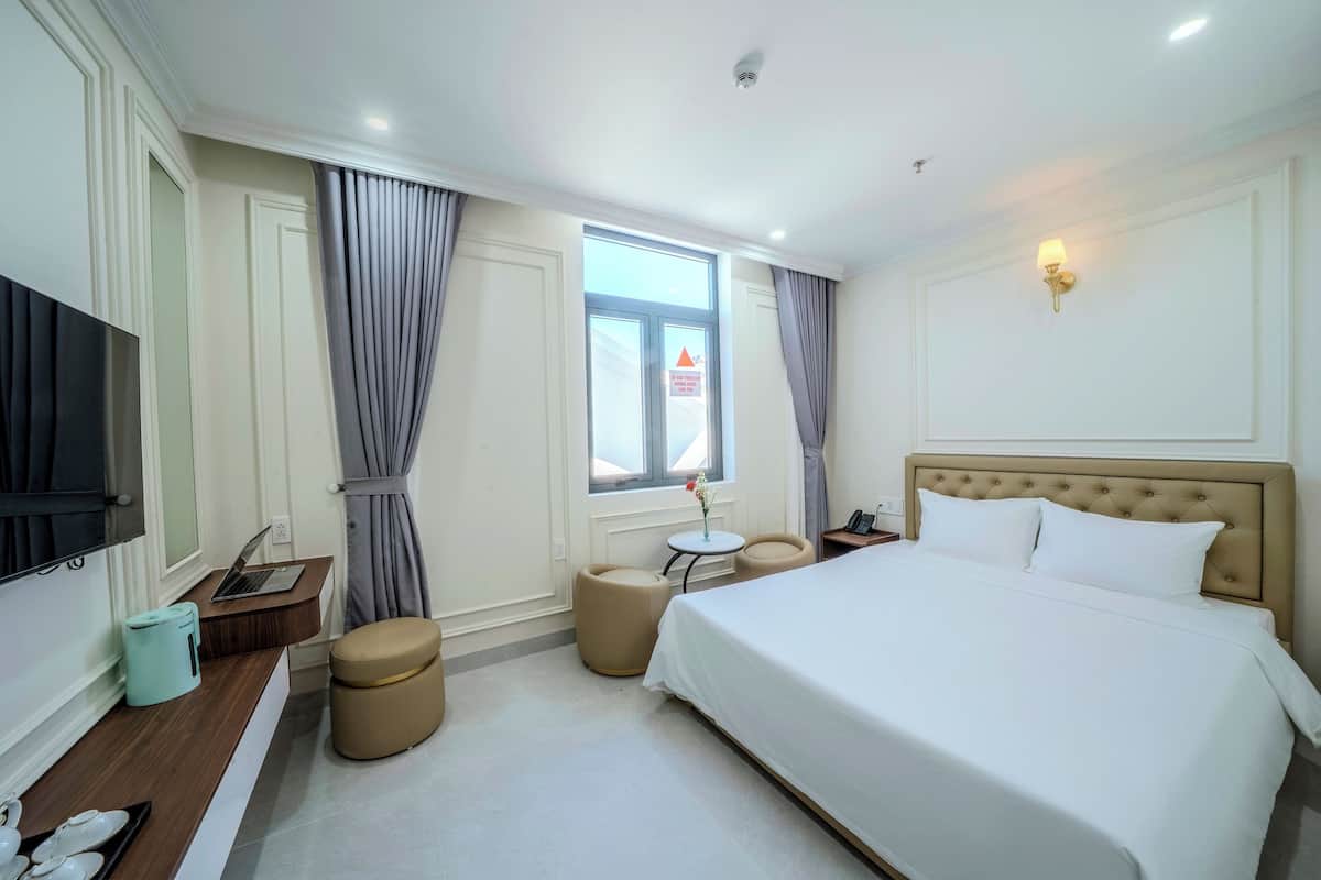 A hotel room with a large bed, a desk with a laptop, a small round table, and a TV.