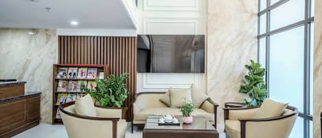 A lobby with a sofa, armchairs, a coffee table, a bookshelf, and a large window.