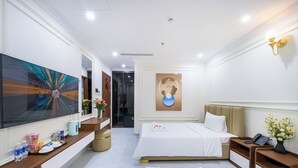 A hotel room with two beds, a large artwork on the wall, a modern light fixture, and a small table with amenities. - Tourane Boutique Hotel (Da Nang)