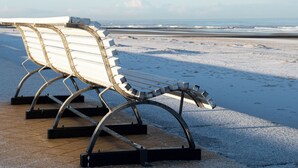 A row of metal and wooden beach chairs on a sandy beach with a view of the ocean. - Let's Go Raversijde (Oostende)