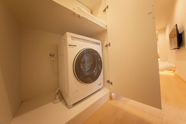 A compact, white washing machine in a small, enclosed laundry area with a wooden floor. - HOTEL SHITAMACHI PLACE ASAKUSA (Taito-ku)