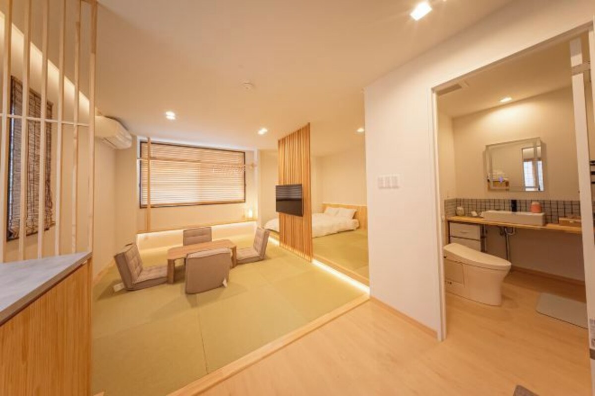 A modern hotel room with a sofa, a small table, a TV, and a bathroom with a sink and toilet.