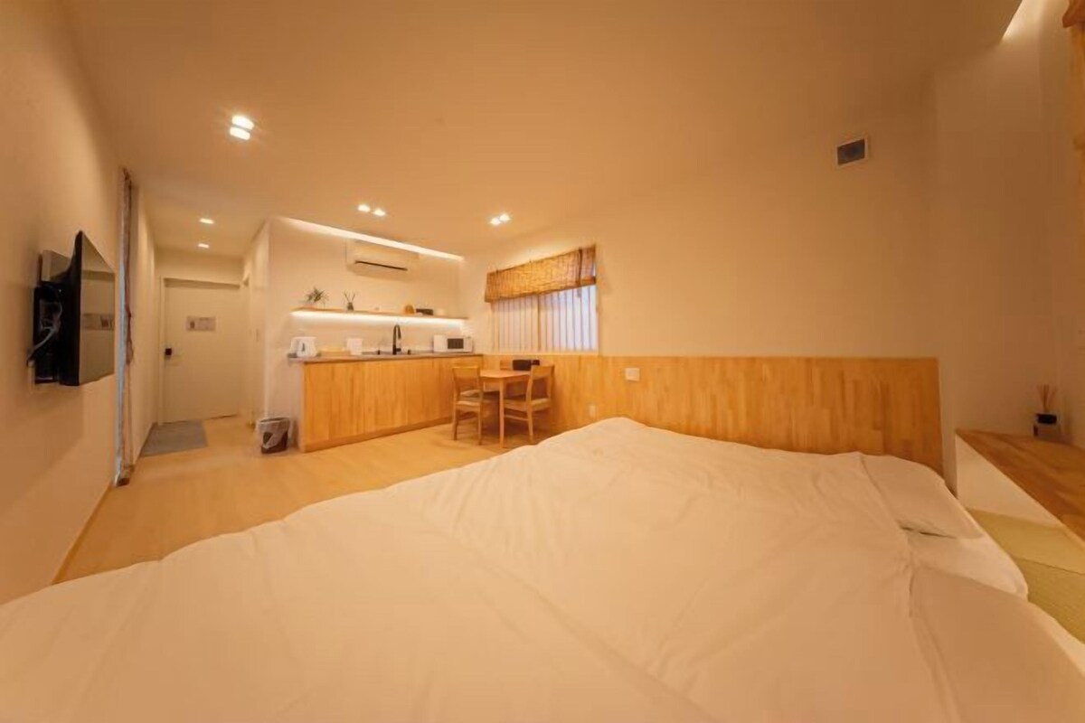 A hotel room with a large bed, a small desk, and a kitchenette area.