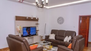 A modern living room with a sofa, two armchairs, a coffee table, a TV, and a clock on the wall.