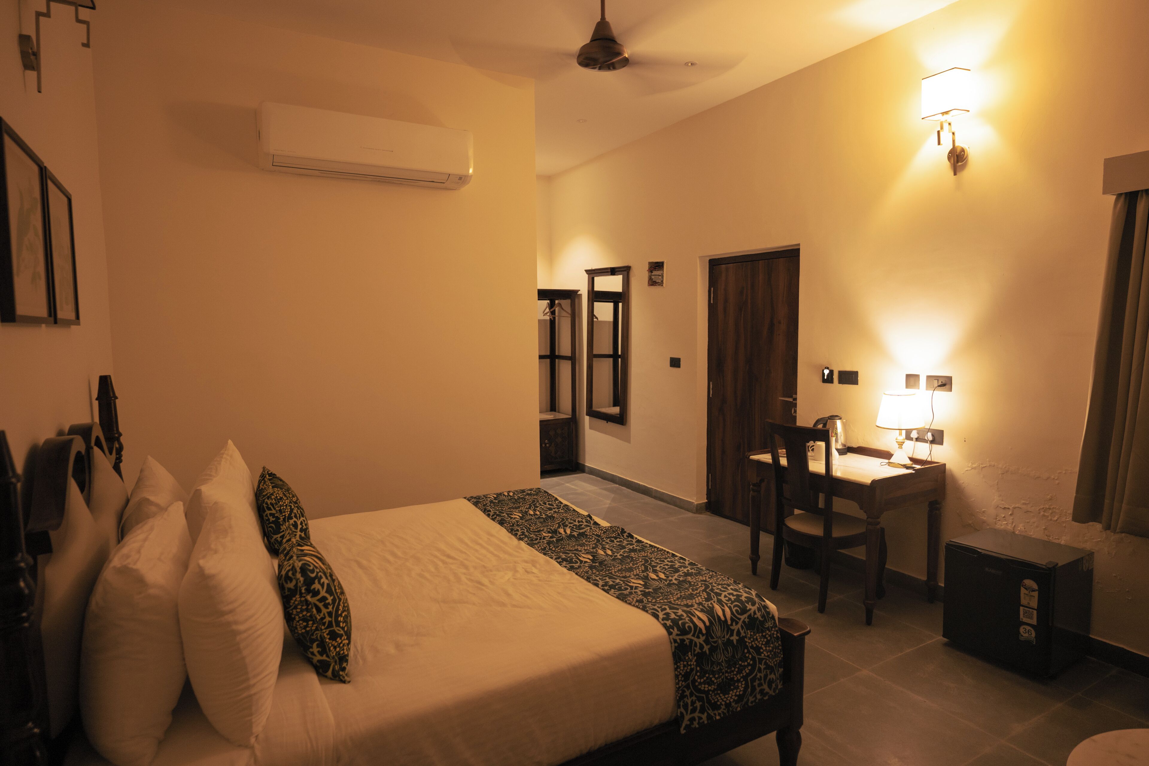 A hotel room with a bed, a desk, a chair, and a small refrigerator.