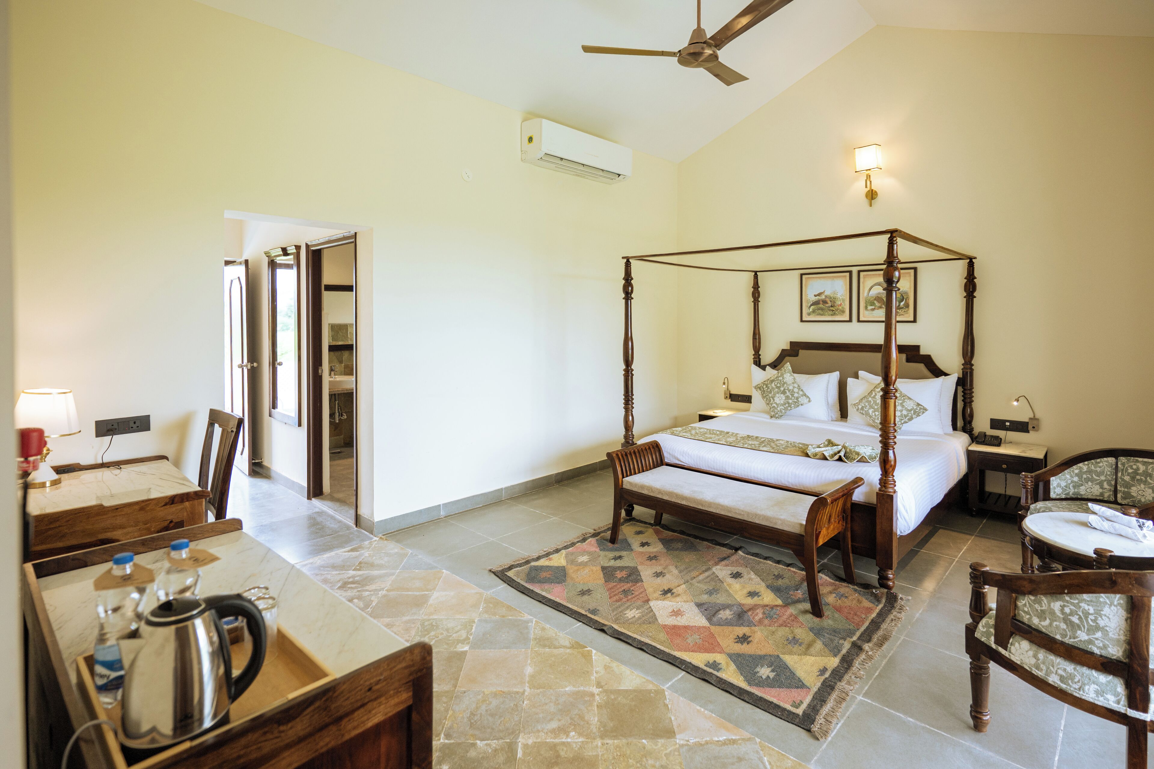 A spacious bedroom with a four-poster bed, a wooden desk with a kettle, and a chair.