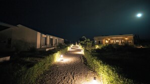 A nighttime pathway leading to a building with illuminated windows and a visible moon in the sky. - Nature Jawai Retreat | Luxury Private Pool Villa Resort, Jawai (Bali)