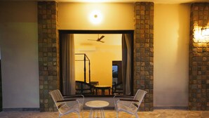An outdoor patio with two metal chairs and a small round table, a stone wall, and a ceiling fan. - Nature Jawai Retreat | Luxury Private Pool Villa Resort, Jawai (Bali)