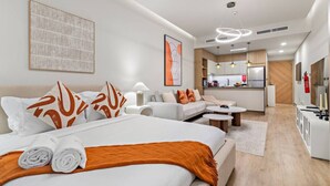 A modern hotel room with a large bed, a sitting area with a sofa, a small table, and a kitchenette in the background. - FIRST CLASS | Studio | Minimalist Chic Retreat (JVC)