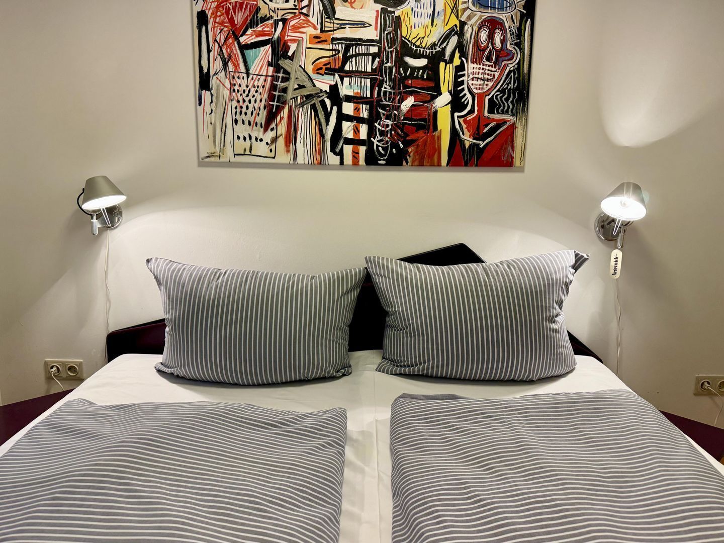 Ein Hotelzimmer mit einem Bett, gestreifte Kissen und einem farbenfrohen, abstrakten Gemälde an der Wand.