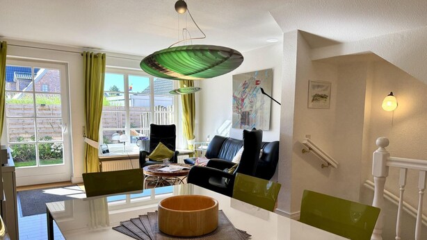 Un salon moderne avec une table à manger blanche, des chaises vertes, un canapé noir et une suspension verte.