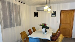 A dining area with a table set for four, surrounded by chairs, a vase with flowers, and a bottle of wine. - Cosy and Comfortable House (Prades)
